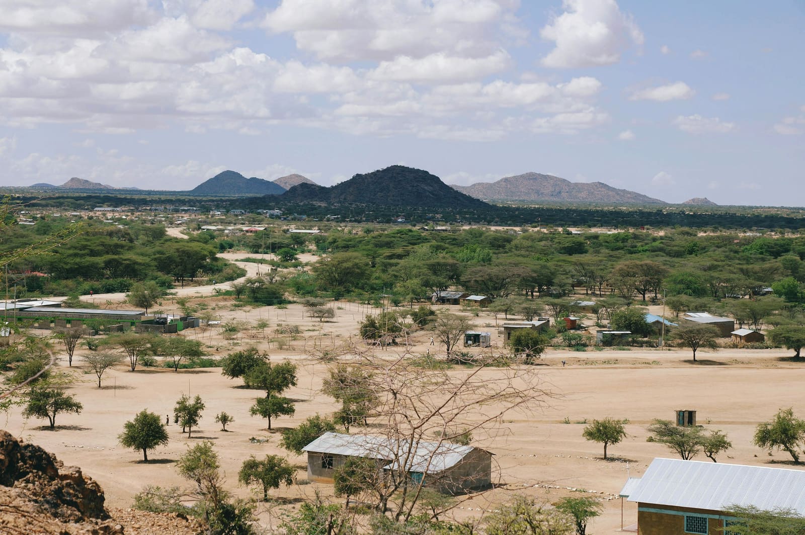 Acacia scrub, sandy ochre ground and scattered tin-roofed buildings below rocky hills in Turkana County, northern Kenya