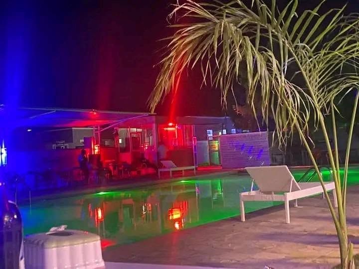 The pool at Cherinas Homes at night, lit in red and green, with loungers and a palm in the foreground.